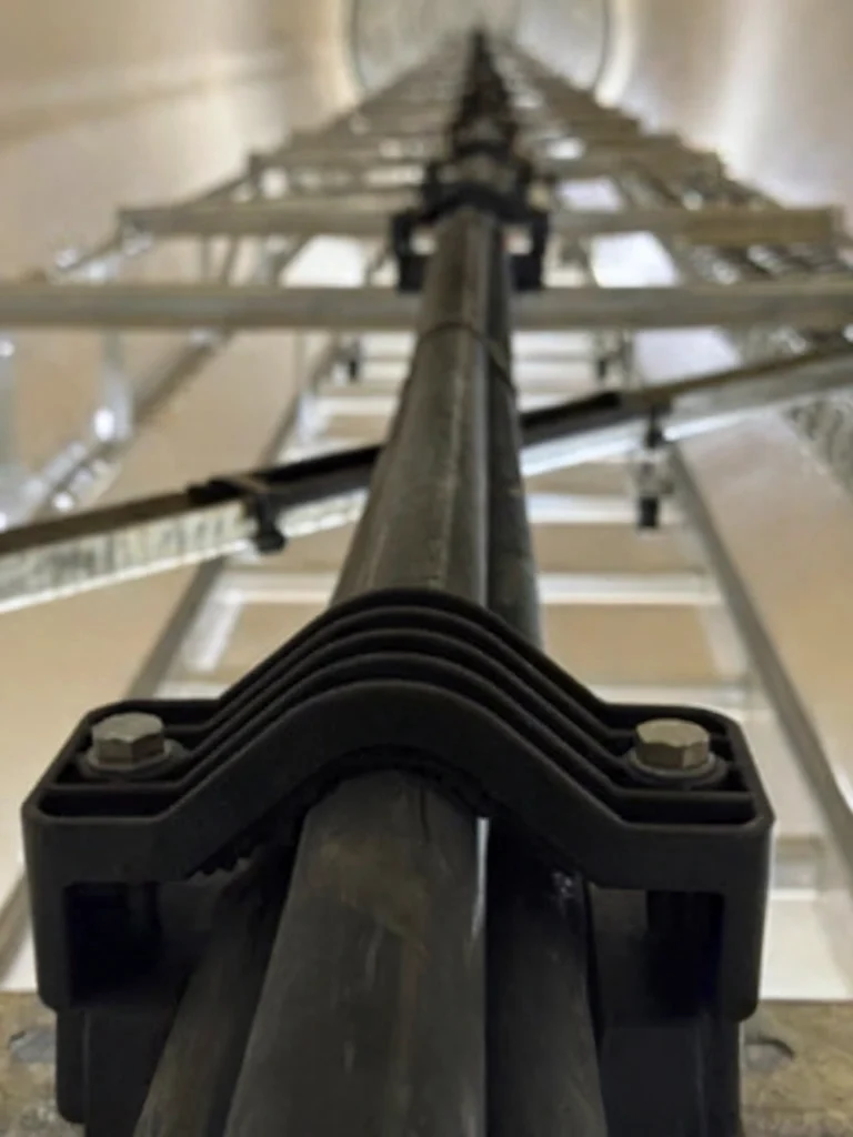 Close-up of ïd-Technik cable clamps holding MV electrical cables along a vertical ladder rack within a high-voltage infrastructure environment.